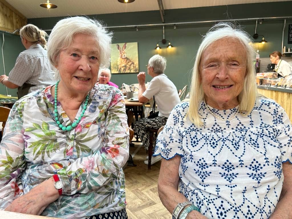 Two elderly women smiling and sitting in a cafe environment