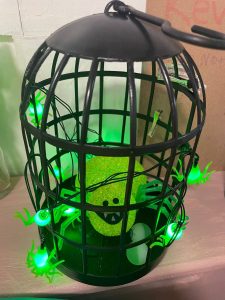 Halloween cage decoration with green spider lights and a glittery green monster inside.