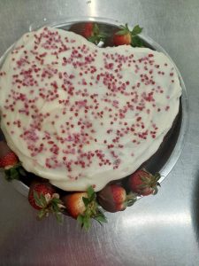 Heart-shaped Valentine's cake with white frosting, heart sprinkles, and chocolate-covered strawberries.